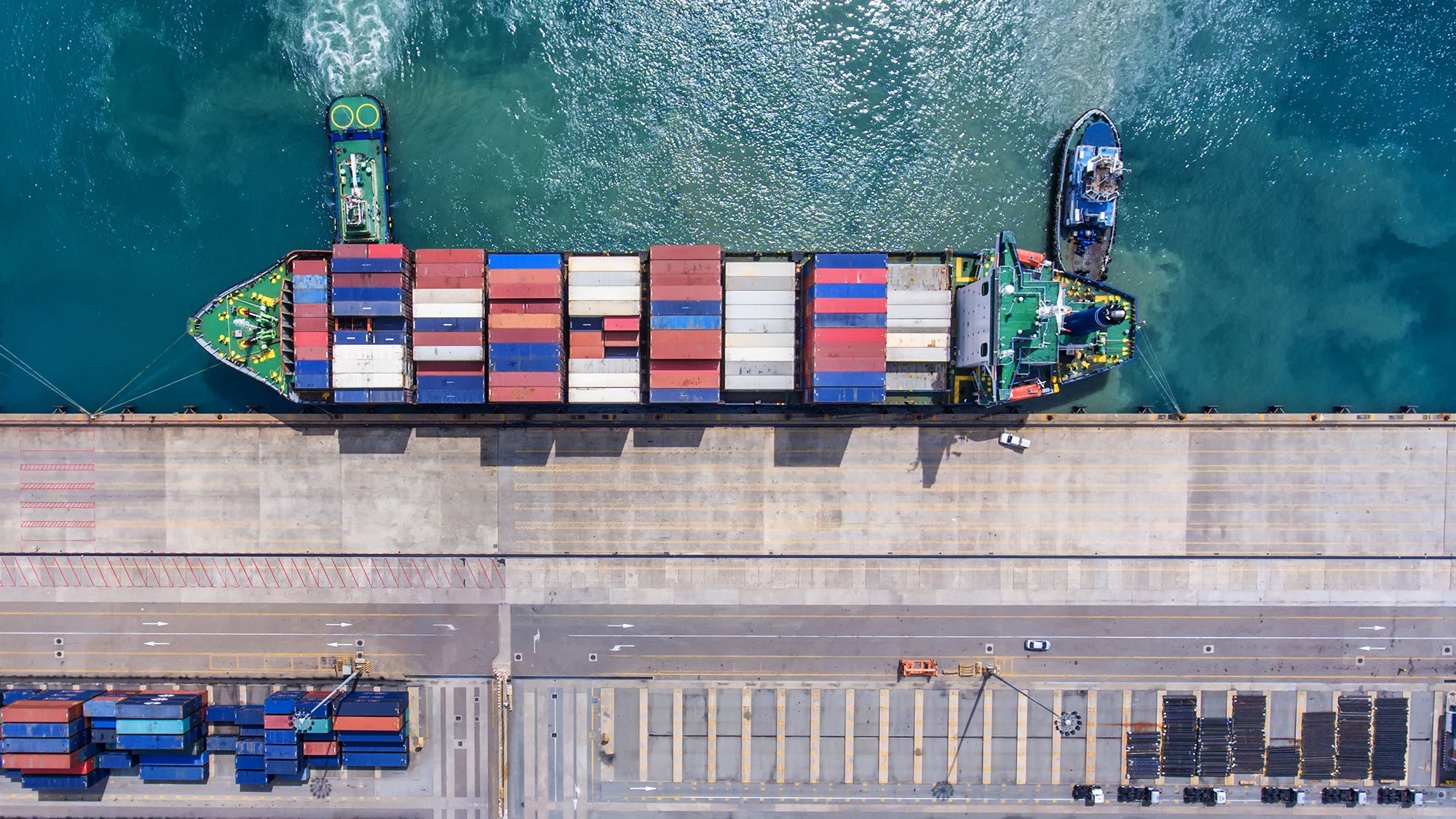 Aerial view of a cargo ship docked at a port with colorful shipping containers on board and trucks nearby