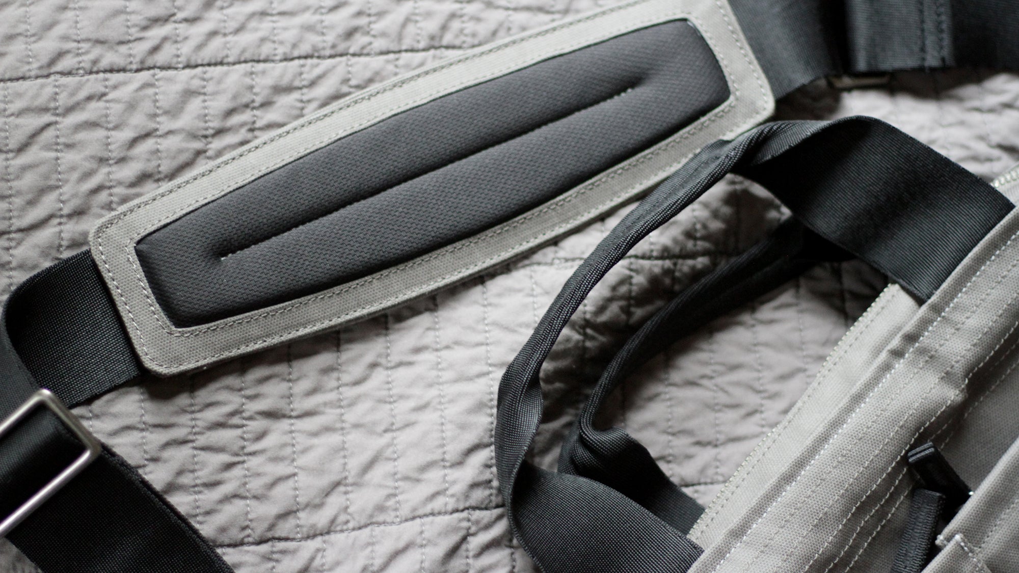Close-up of padded straps and handles on a gray quilted fabric surface, showing detailed stitching and material texture.