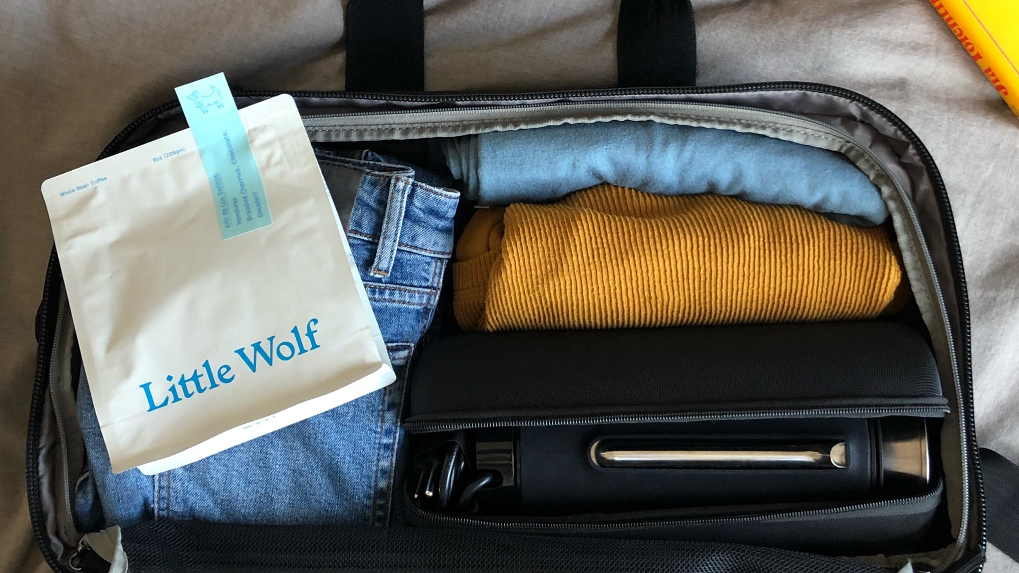 A packed V1 Grandcart One with folded clothes and a white coffee bag labeled 'Little Wolf' with a blue sticker reading 'With the same roasting method, organic, chocolate, balanced'.