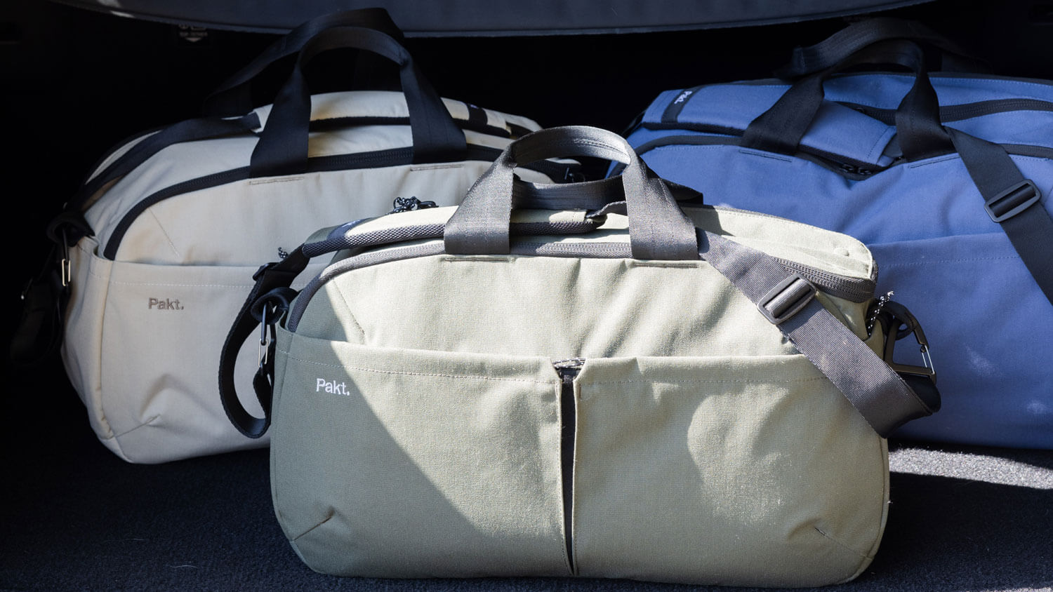 Three Grandcart One Travel Duffels in Sand, Forest, and Ocean with black handles and shoulder straps, two bags have the brand name 'Pakt.' visible on the front pocket.