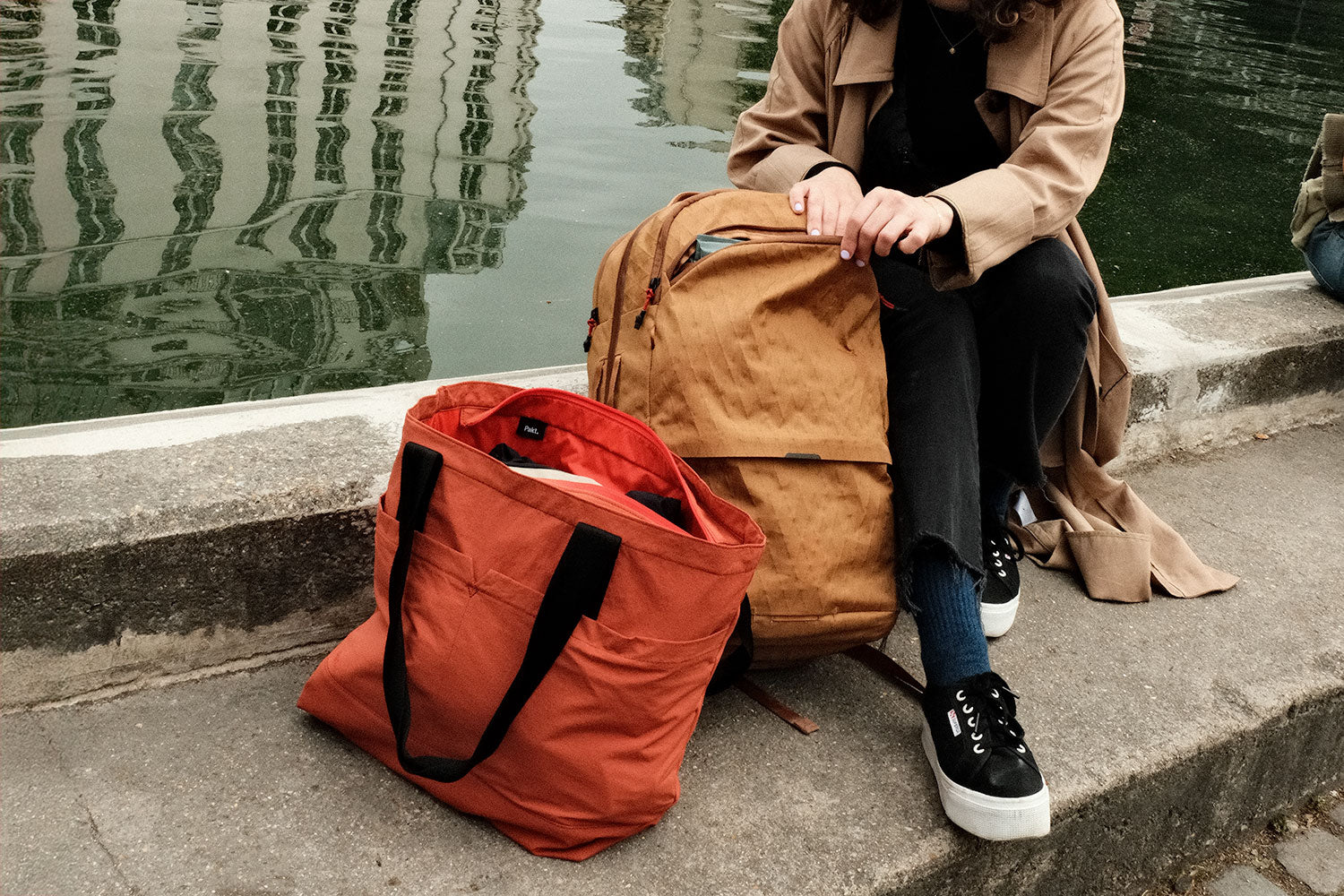 Woman looking for something inside the Aero Travel Backpack alongside a river