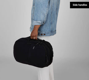 Everyday 22L black backpack held by a hand at its side handle — Side handles