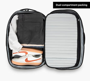 An open Travel Backpack showing neatly packed clothes and shoes with label 'Dual-compartment packing'