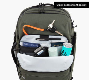 Green travel backpack with open quick-access front pocket showing passport, keys, a can, and other travel items