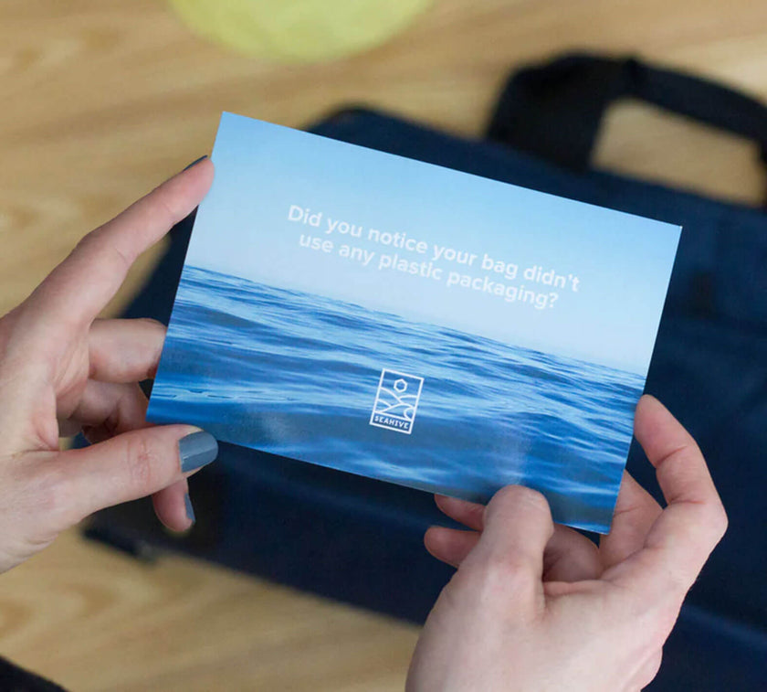Hands holding a card showing ocean waves with text: "Did you notice your bag didn't use any plastic packaging?" and a SEAHIVE logo below.