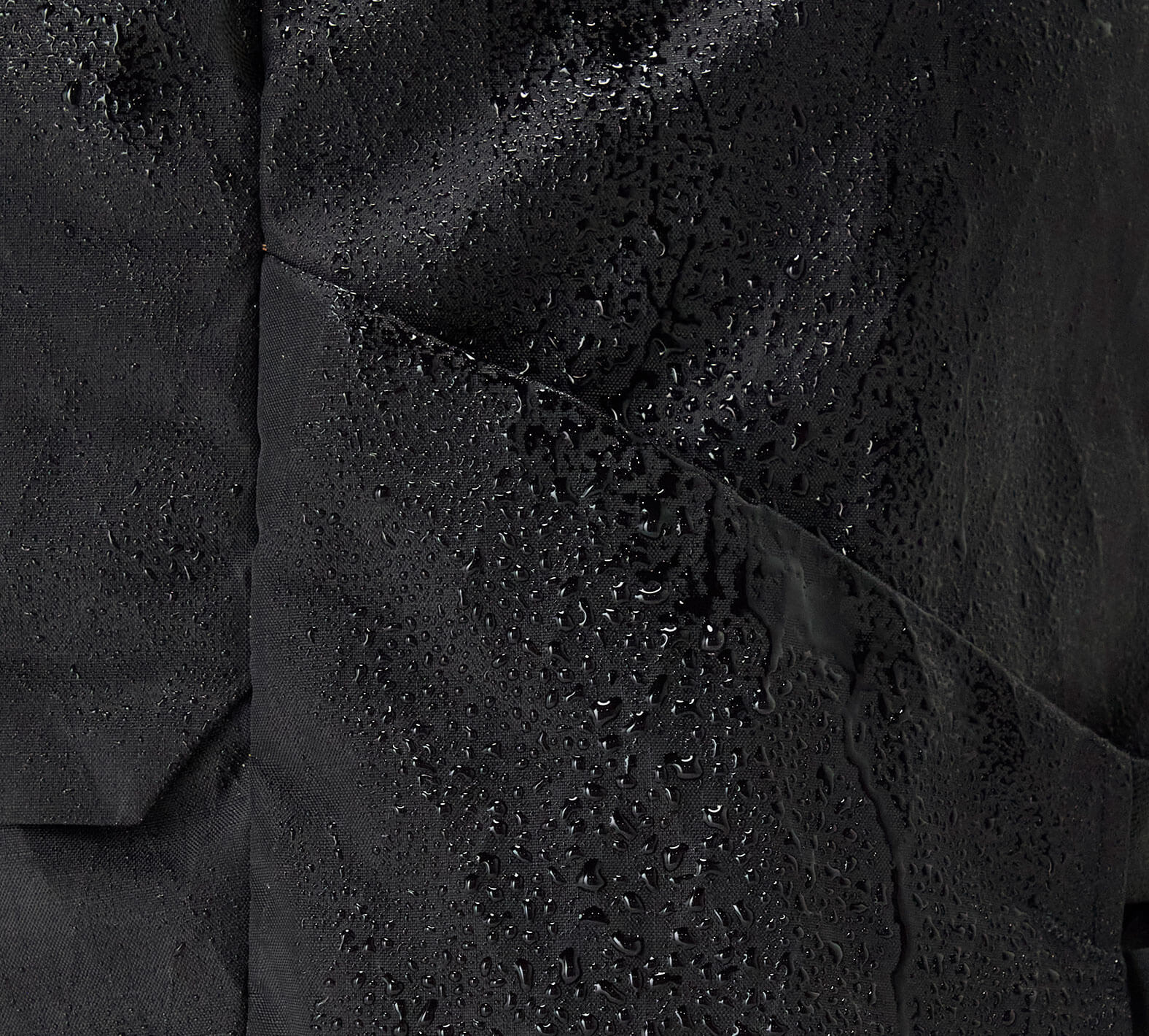 Close-up of black Aero Travel Backpack material with water droplets showing water resistance.