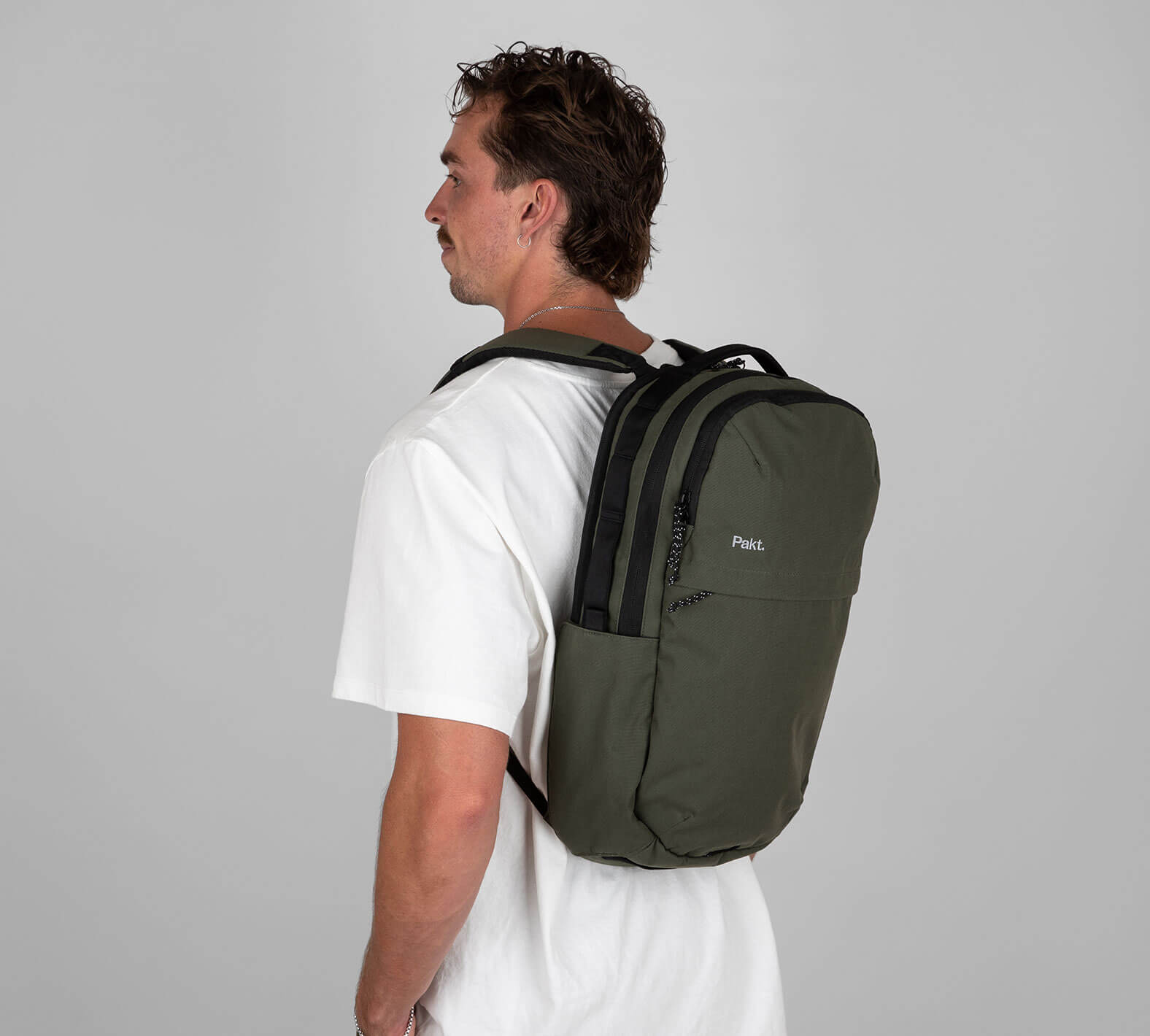 Side view of a man wearing an olive-green 22 L backpack with two zippered compartments and padded shoulder straps.
