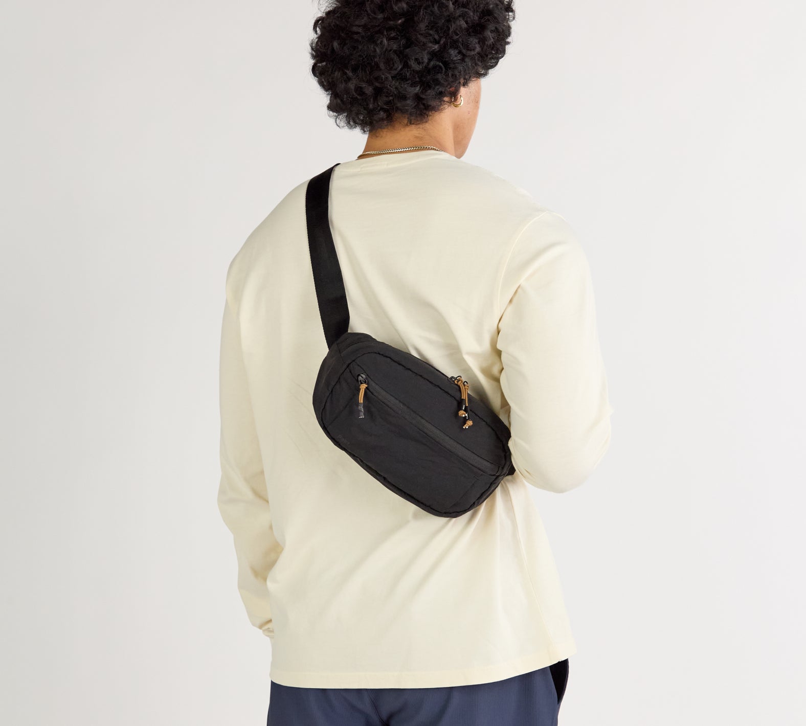 Black Stash Sling crossbody bag worn across the back over a cream long-sleeve shirt