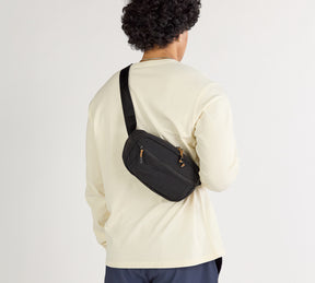 Black Stash Sling crossbody bag worn across the back over a cream long-sleeve shirt