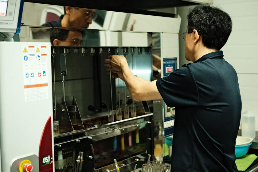 Man in black shirt operating a laboratory machine with multiple test tubes filled with colorful liquids