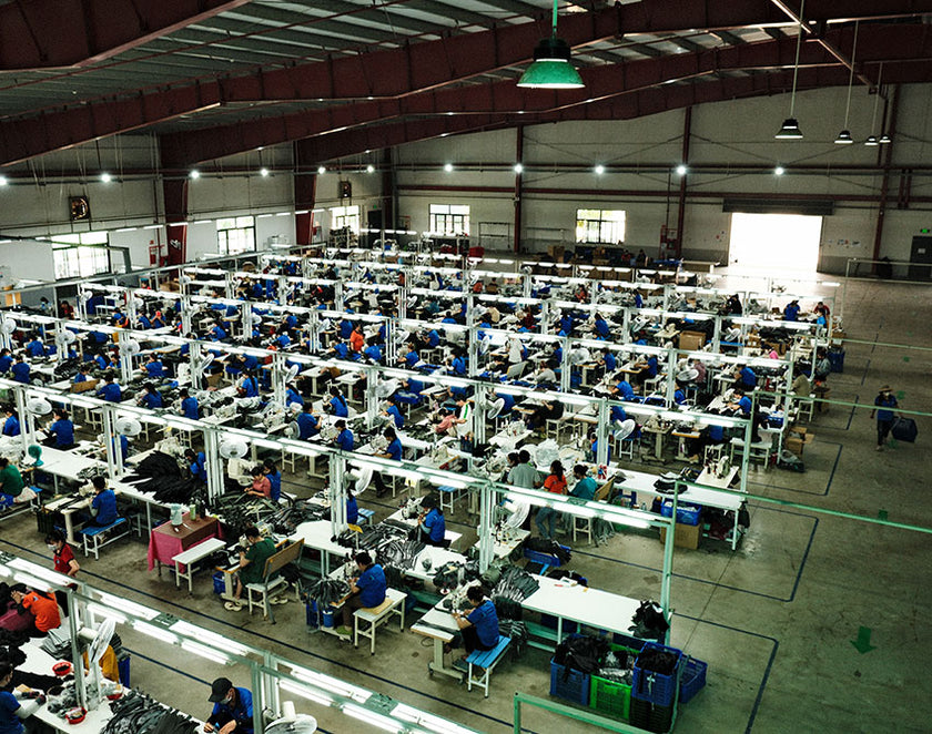 Large factory floor with rows of workers operating sewing machines under industrial lighting.