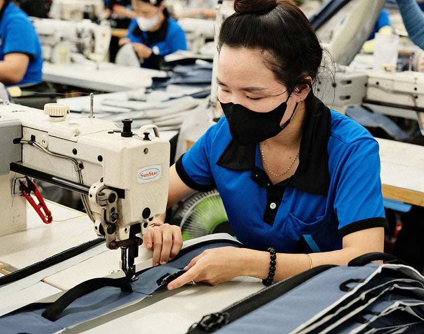 Woman wearing a black mask and blue shirt sewing fabric on a SunStar sewing machine in a factory setting