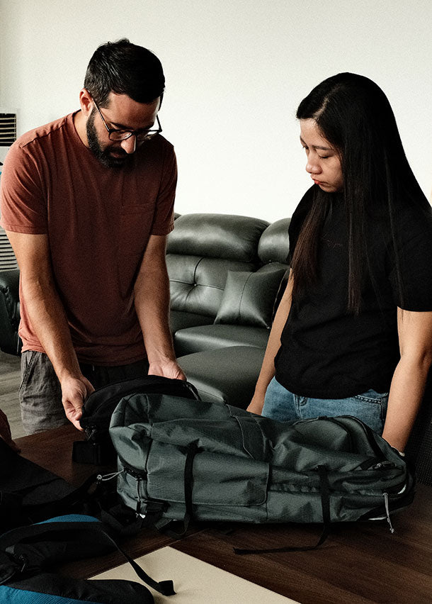 Two people, a man and a woman, standing by a table looking at a large green backpack.