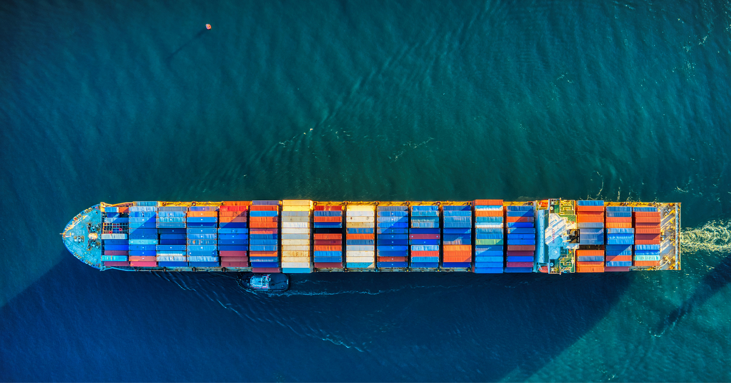Aerial view of a large container ship loaded with colorful shipping containers sailing on blue water.