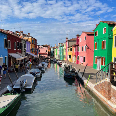 Canal lined with colorful buildings and boats under a partly cloudy sky.