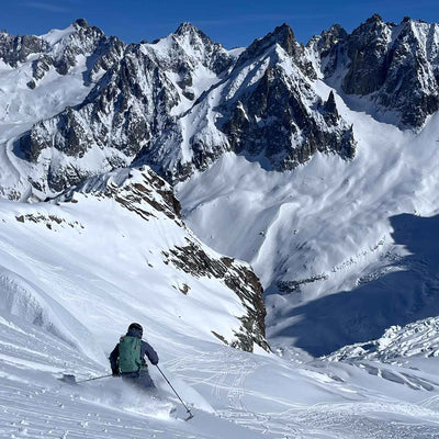 Skier descending a steep snow slope toward rugged alpine peaks under a clear blue sky