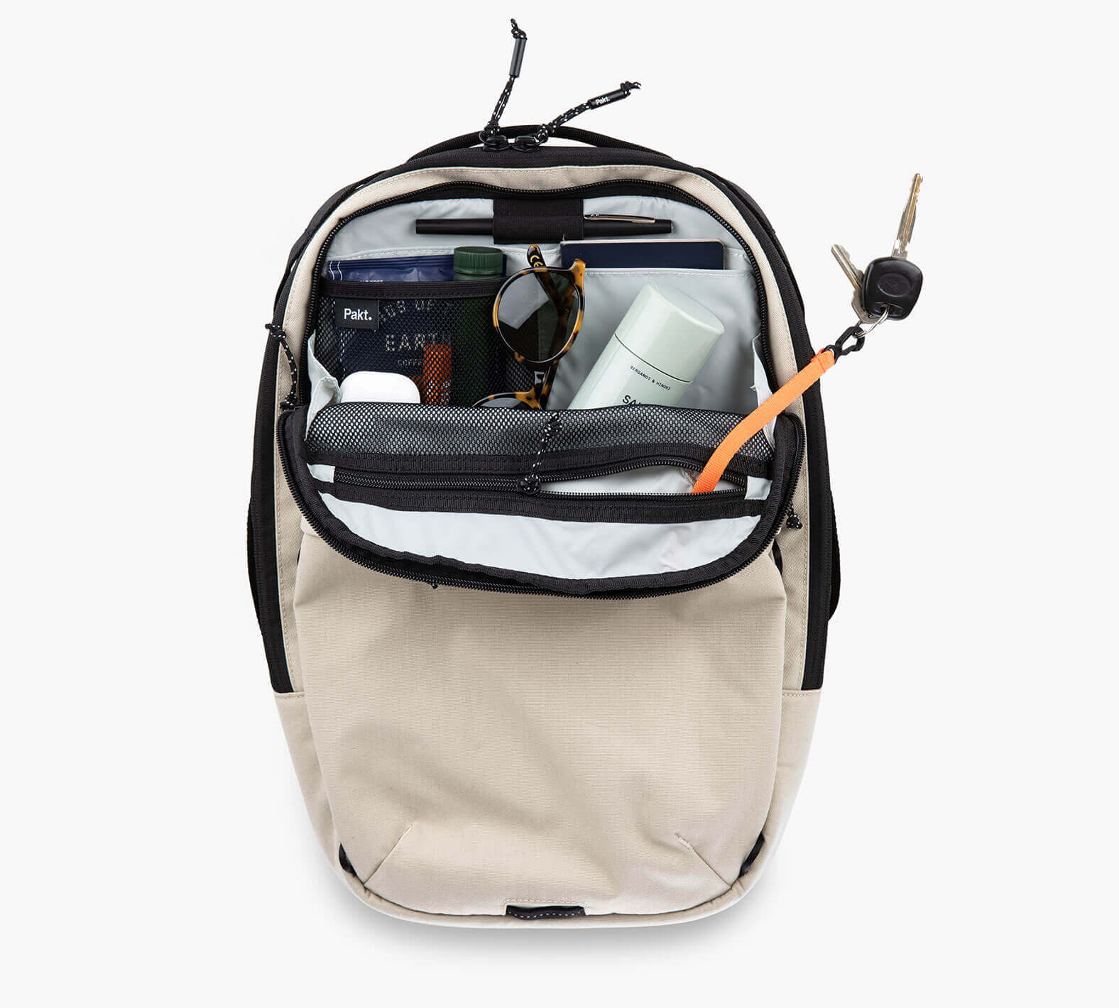 The sand colored Everyday 22L Backpack open showing contents including sunglasses, a book, a water bottle, and a small pouch