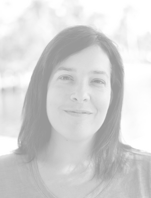 Black-and-white portrait of a woman with shoulder-length dark hair, smiling gently, outdoors with blurred background.