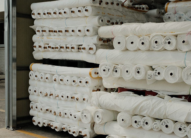Stacks of white fabric rolls stored in a warehouse, arranged in multiple horizontal layers.