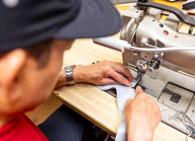 Person sewing light blue fabric on an industrial sewing machine, focusing on hands and machine details.