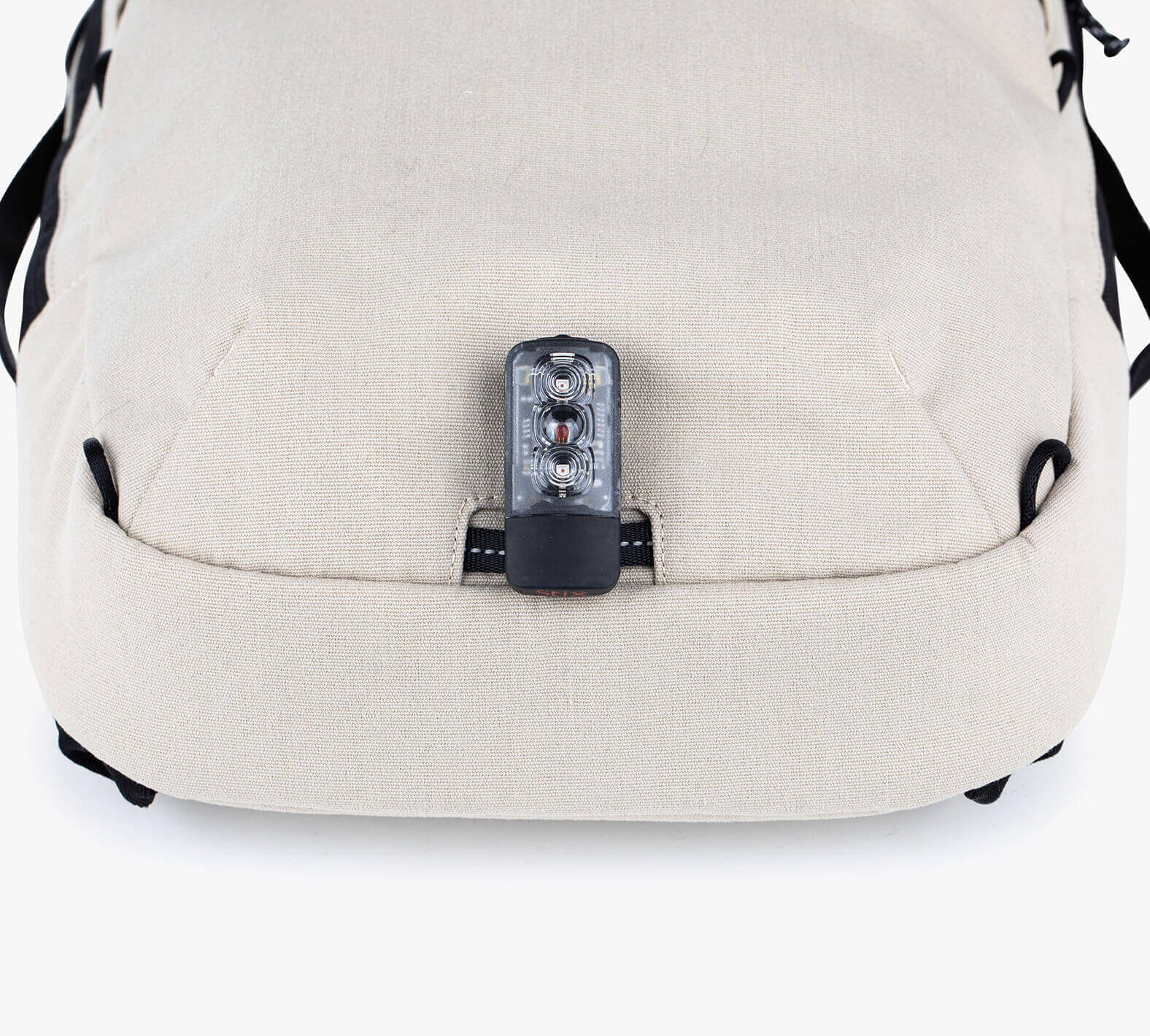 Close-up of the bottom front of a beige sling backpack with a small black and transparent device attached.