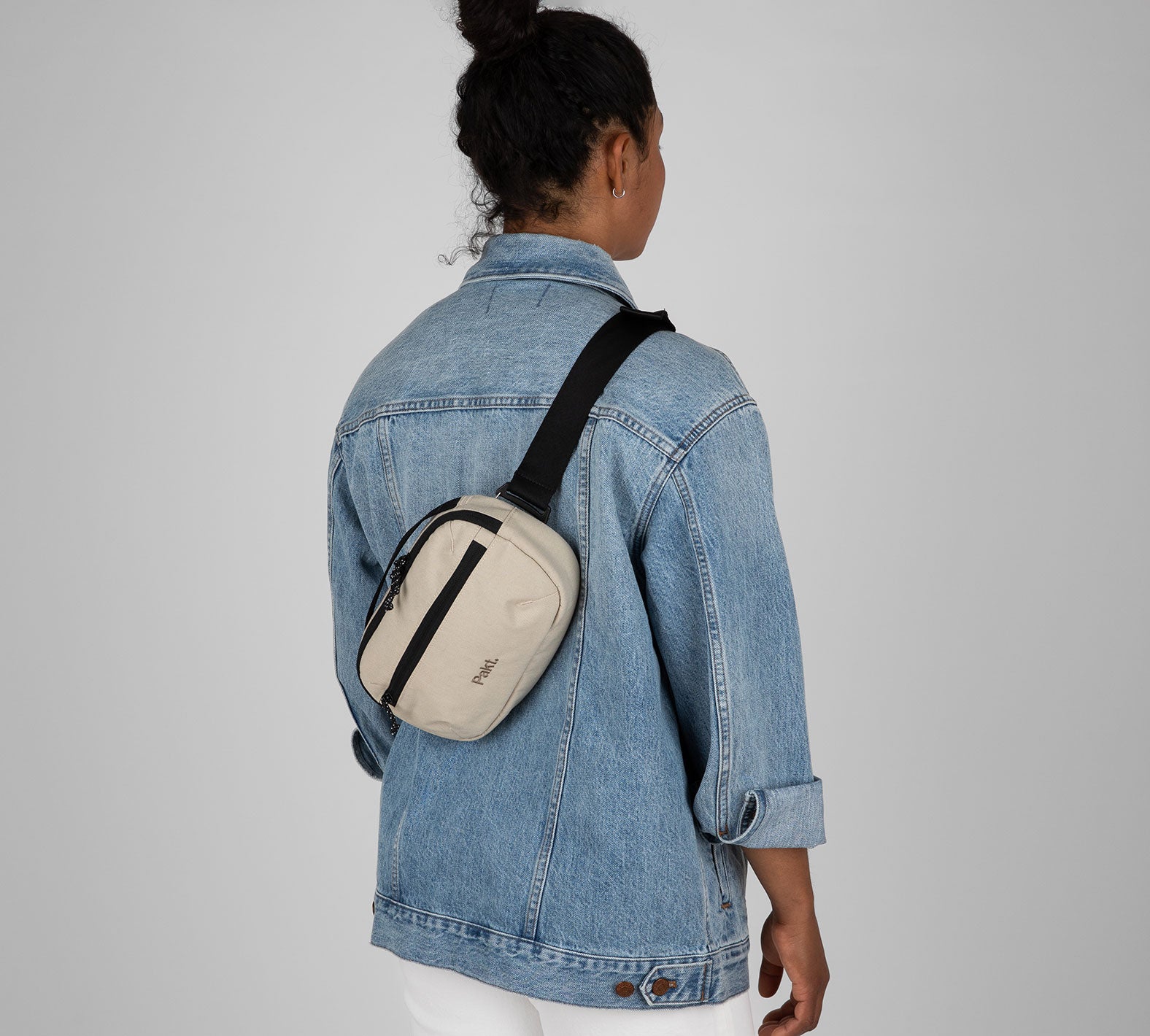 Person wearing beige Everyday 3L sling bag crossbody over a denim jacket; black strap and front zipper pocket.
