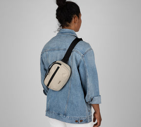 Person wearing beige Everyday 3L sling bag crossbody over a denim jacket; black strap and front zipper pocket.