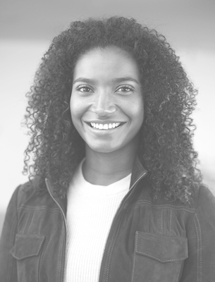 Smiling woman with long curly hair wearing a jacket and light sweater, looking at the camera.