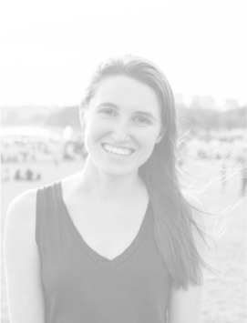 Smiling young woman with long hair standing outdoors on a beach or park with blurred people in the background
