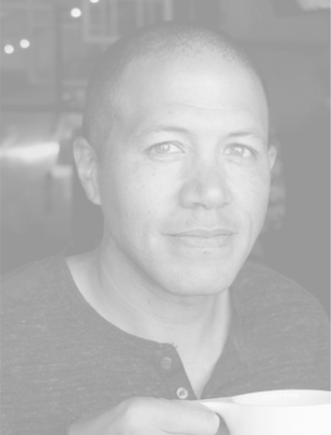 Man holding a coffee cup, looking at camera; close-up black-and-white head-and-shoulders portrait.
