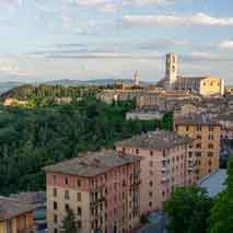Hillside town view with apartment buildings in foreground, trees, and a cathedral tower under a partly cloudy sky.